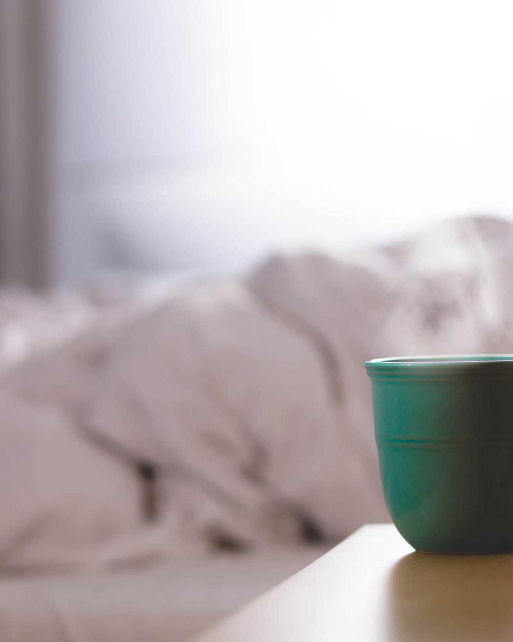 Morning light on linen sheets beside a green mug
