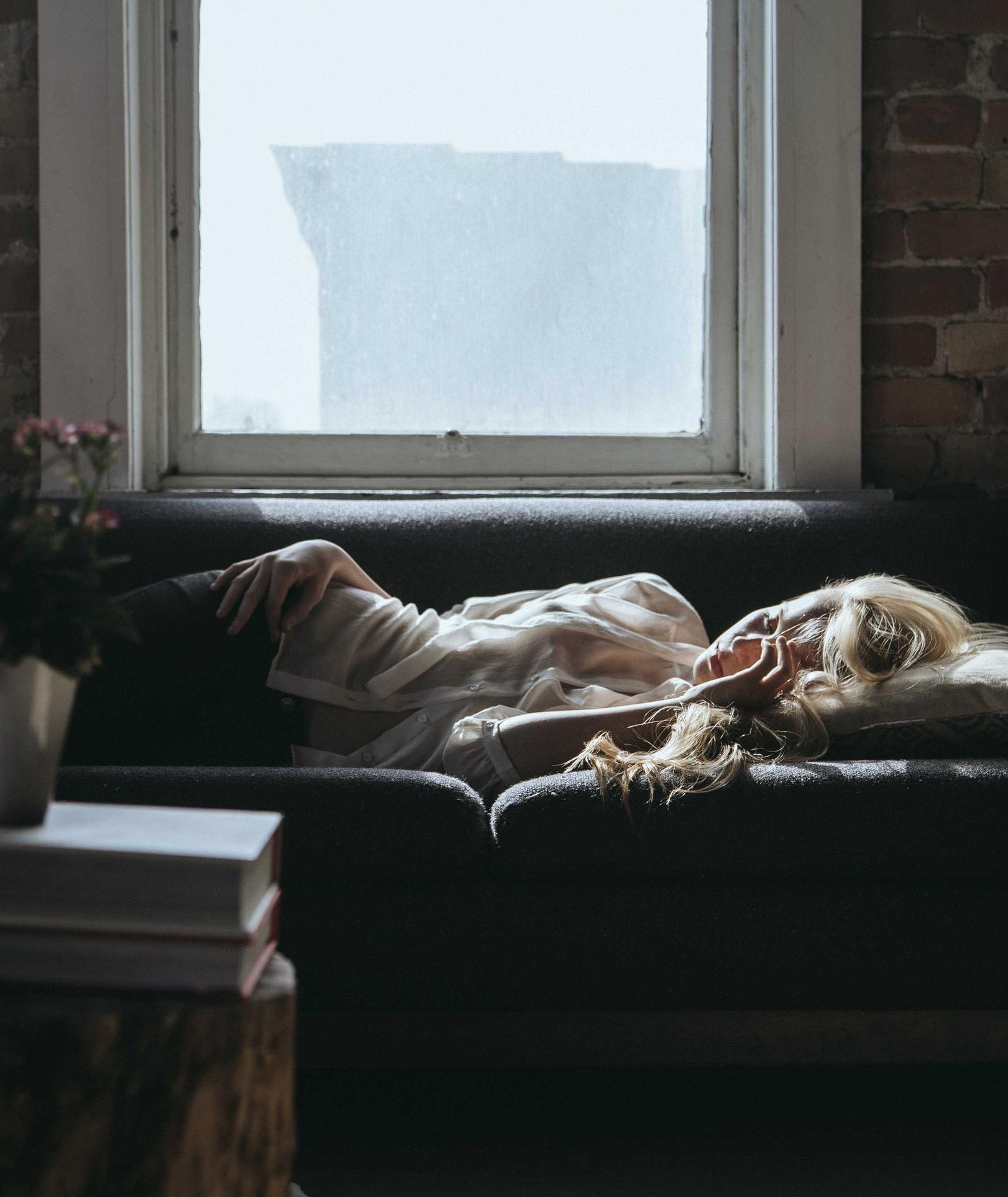 A guest asleep on a sofa beside a tall window